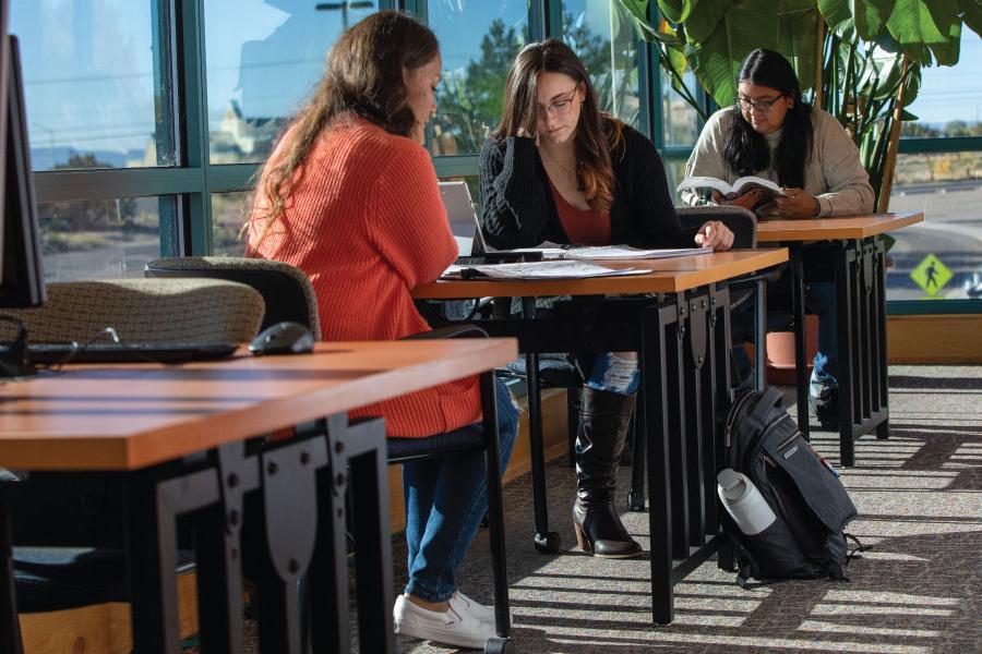 Tres estudiantes sentados en mesas en la biblioteca.